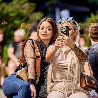 Zwei junge Frauen posieren fröhlich für ein Selfie vor der Messe Basel – ein spontaner Lifestyle-Moment eingefangen von Bluesun vor der Art Basel.