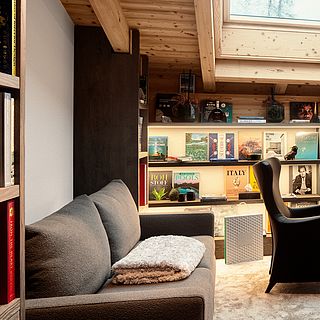 Cozy room under the roof with bookshelf, sofa and designer armchair - interior design photography by Bluesun with a focus on light and atmosphere.