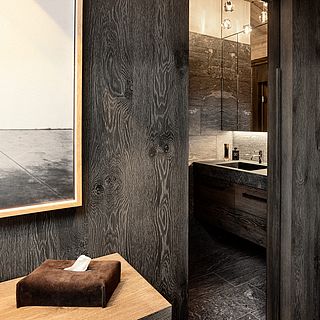 A modern bathroom with dark wood paneling, natural stone washbasin and mirror - photographed for interior design clients of Bluesun.