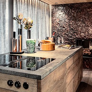 Close-up of a stylish kitchen with dark natural stone worktop, artistic copper wall and elegant decoration - professionally photographed by the Bluesun Interior Design Team.