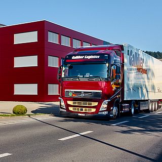Red Galliker Volvo truck with white trailer exiting company premises, photographed for Galliker Transport AG.
