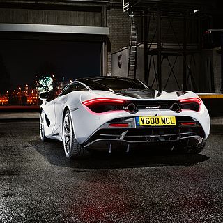 Professional exhibition photography by the Bluesun photo team: white McLaren 720S at night in an industrial setting, with glossy asphalt and atmospheric lighting for impactful presentations.