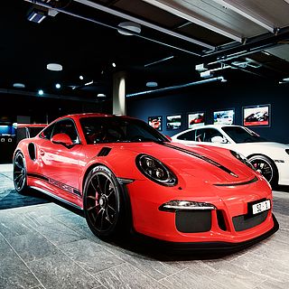 High-end exhibition photography by Bluesun: red Porsche GT3 RS in a stylish car showroom with atmospheric lighting and a dynamic, sporty mood.