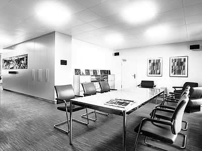 Diagonal view inside the Bluesun studio with a large meeting table, comfortable chairs, a bookshelf with inspiring works, screens, and stylish artwork on the wall – a space for collaboration and creative thinking.