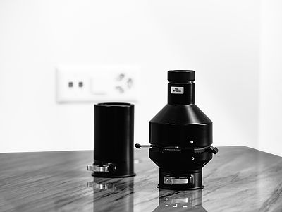 Stylish close-up of Broncolor accessories: projection attachment for lines and gobos, plus a honeycomb grid adapter, placed on a quartzite table in the studio.