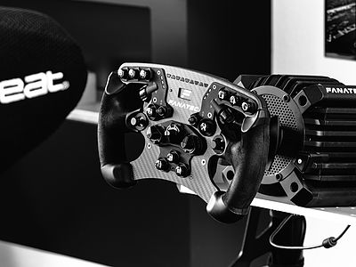 Gros plan sur un volant de course FANATEC haut de gamme avec base direct drive et nombreux boutons – pour des pauses créatives et des moments de détente au studio Bluesun.